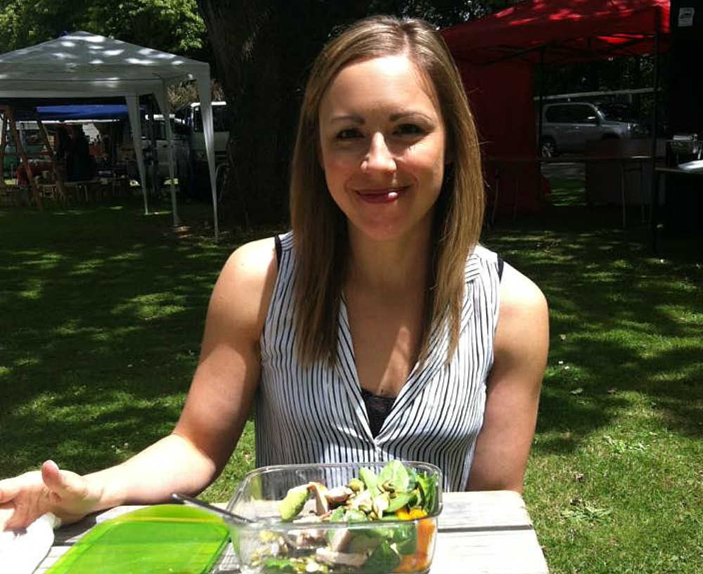 lady sitting in a park eating salad from a glass container